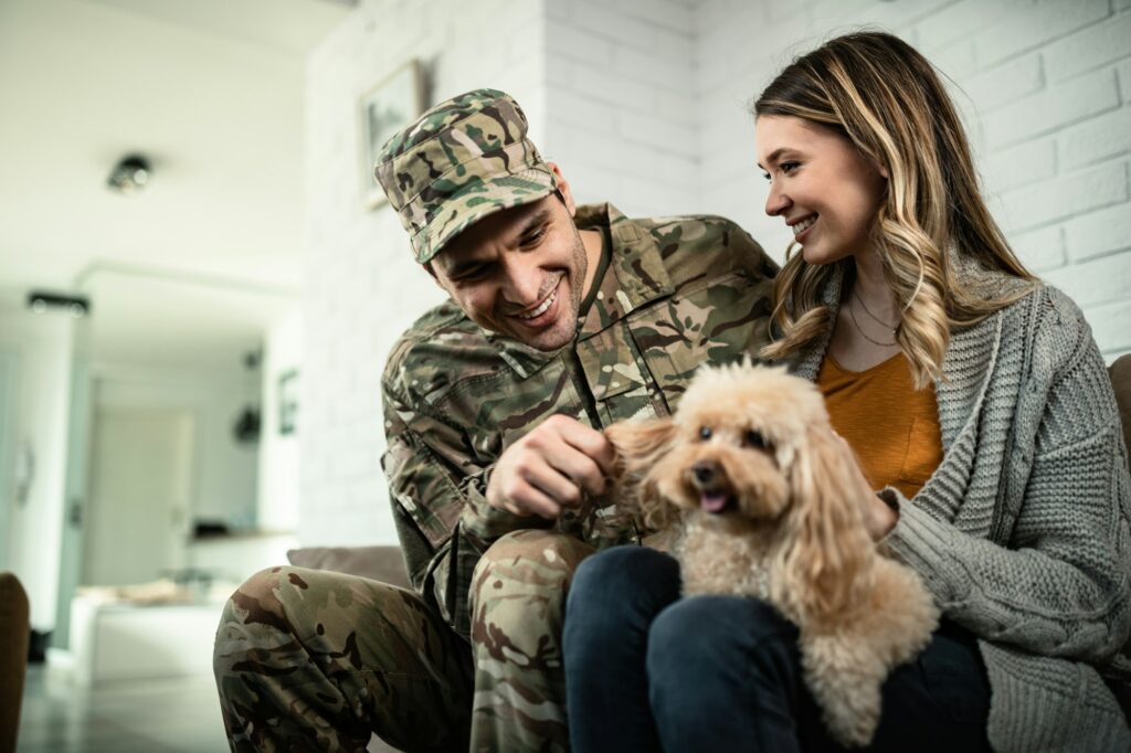 Happy military couple having fun with their dog at home.